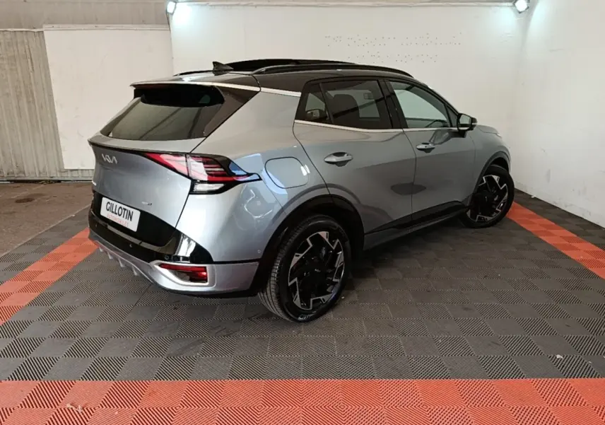 Vue 3/4 arrière droite d'un KIA SPORTAGE gris clair avec toit noir et jantes noires au design moderne.