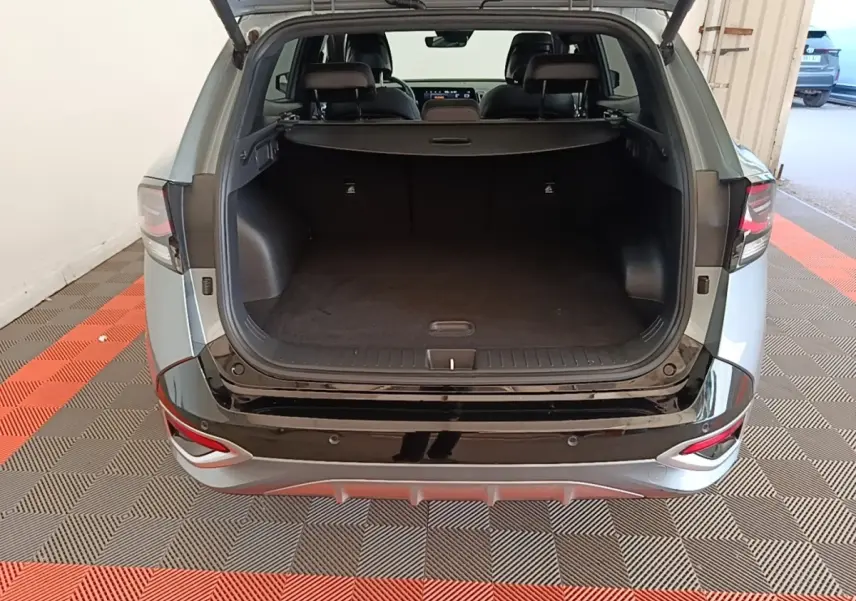 Vue arrière ouverte du Kia Sportage gris clair 2022 montrant le coffre spacieux et la finition noire brillante du pare-chocs.