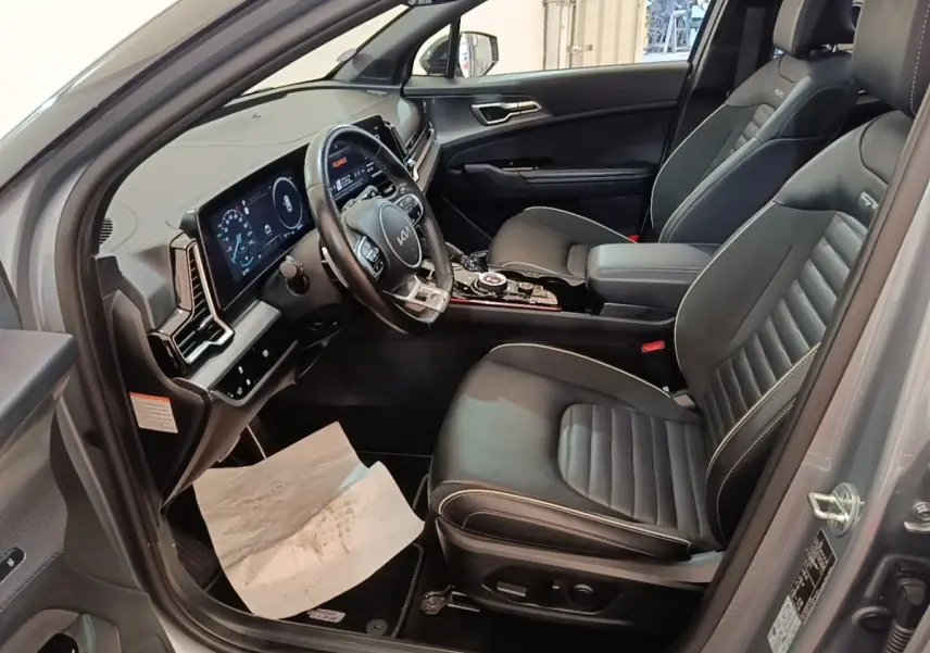 Vue intérieure côté conducteur du Kia Sportage 2022 avec sièges cuir noirs et tableau de bord digital lumineux.