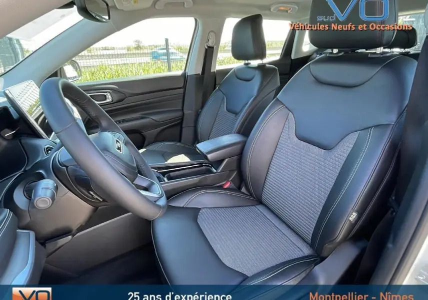 Vue intérieure côté conducteur du Jeep Compass 2024 blanc, sièges noirs en cuir avec accoudoir central et volant multifonction.