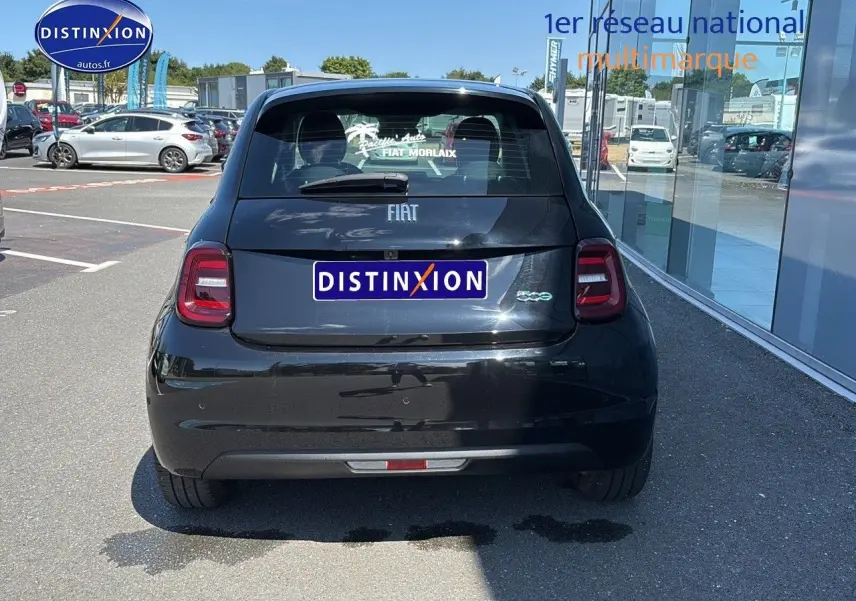 Vue arrière d'une Fiat 500 électrique noire stationnée devant une vitrine avec logo Distinxion sur la plaque.