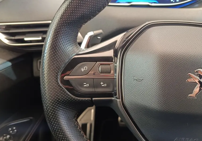 Gros plan sur le volant cuir noir du Peugeot 5008 gris clair, avec commandes audio et logo lion visible.