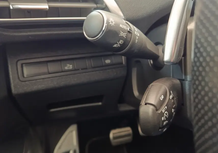 Détail intérieur du Peugeot 5008 gris clair 2019 montrant la commande des phares et le régulateur de vitesse au volant.