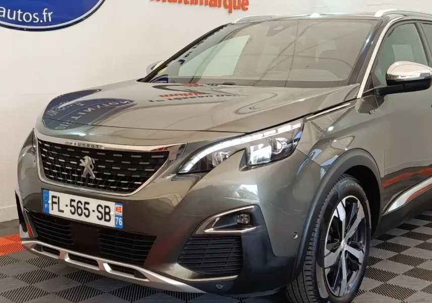 Peugeot 5008 gris clair en 3/4 avant droit, avec calandre chromée et phares LED distinctifs.