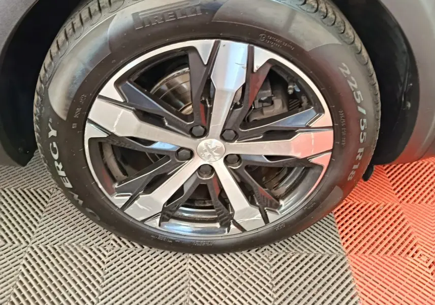 Gros plan sur la roue avant droite gris clair du Peugeot 5008 avec jante alliage noire et argentée, logo lion central visible.
