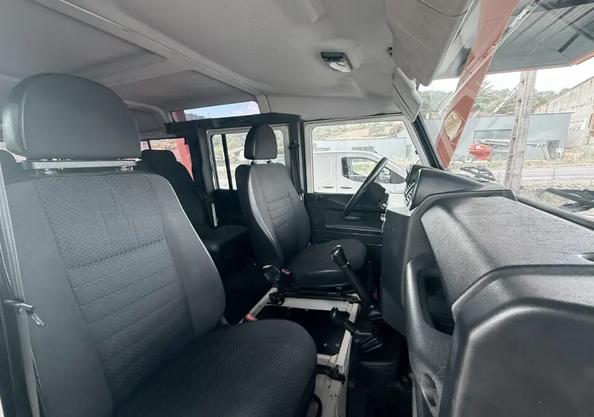 Vue intérieure côté droit du Land Rover Defender 2007, montrant les sièges tissu gris-noir et le tableau de bord noir.