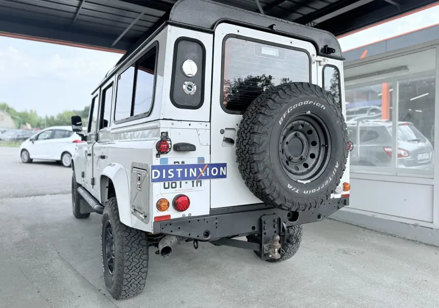 Vue 3/4 arrière droite d'un Land Rover Defender blanc 5 portes avec roue de secours BFGoodrich fixée à l'arrière.