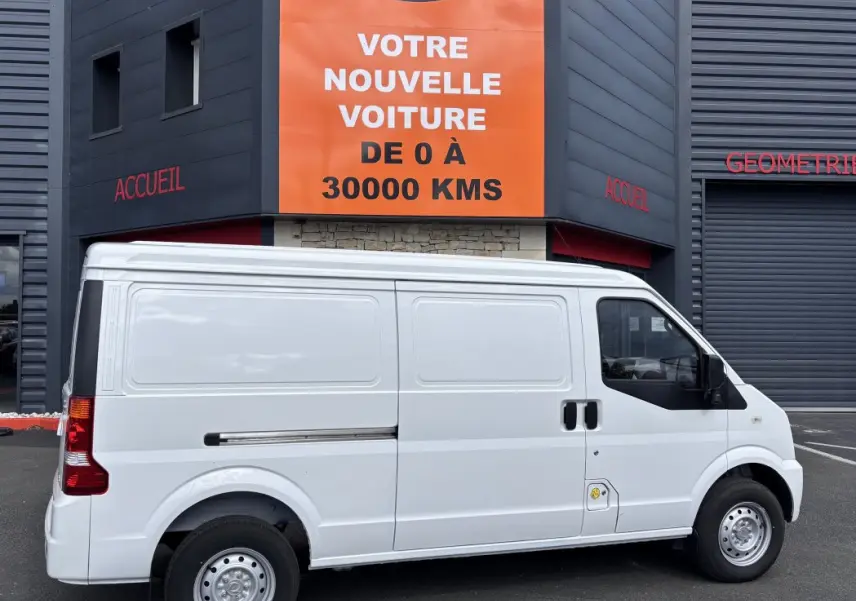 Profil latéral droit du fourgon blanc DFSK EC35 BEV 39KWH, sans fenêtres latérales, garé devant un bâtiment commercial.