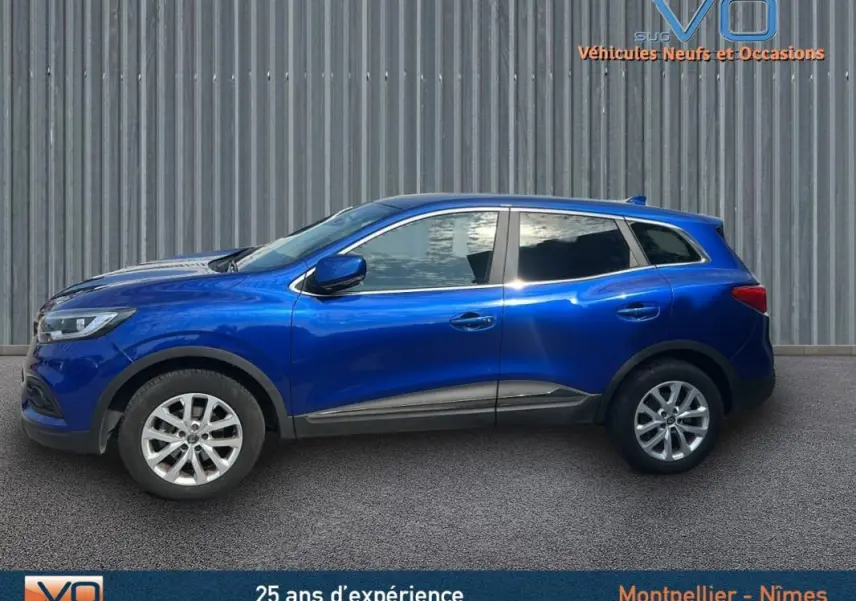 Profil côté gauche d'un Renault Kadjar TCe 140 FAP Business bleu foncé avec jantes alliage et barres de toit visibles.