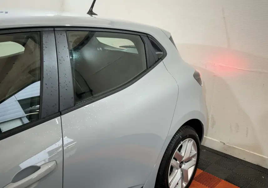 Vue 3/4 arrière droite d'une Renault Clio gris clair 2025 avec jante alliage et antenne toit compacte.