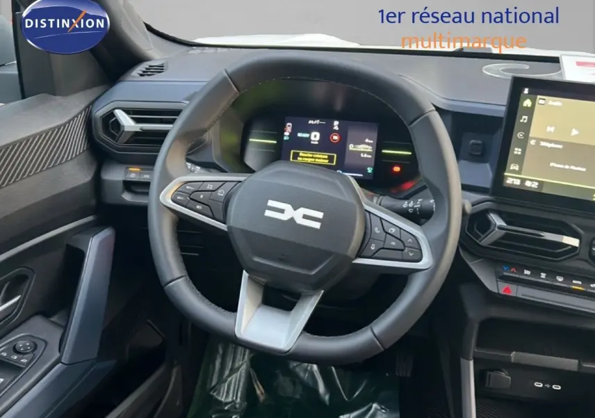 Vue intérieure centrée sur le volant multifonction et le tableau de bord numérique du Dacia Duster blanc Glacier 2025.