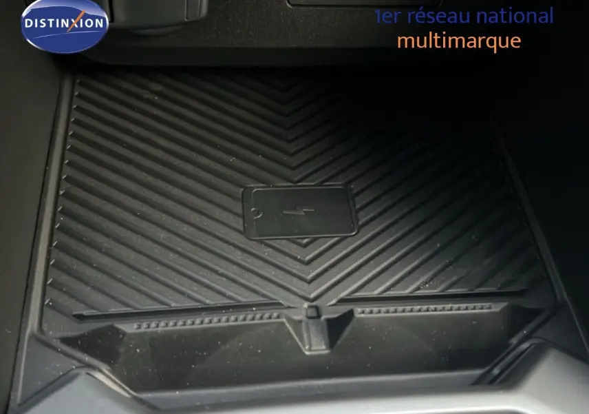 Gros plan sur le chargeur sans fil noir intégré à la console centrale du Dacia Duster blanc glacier 2025.