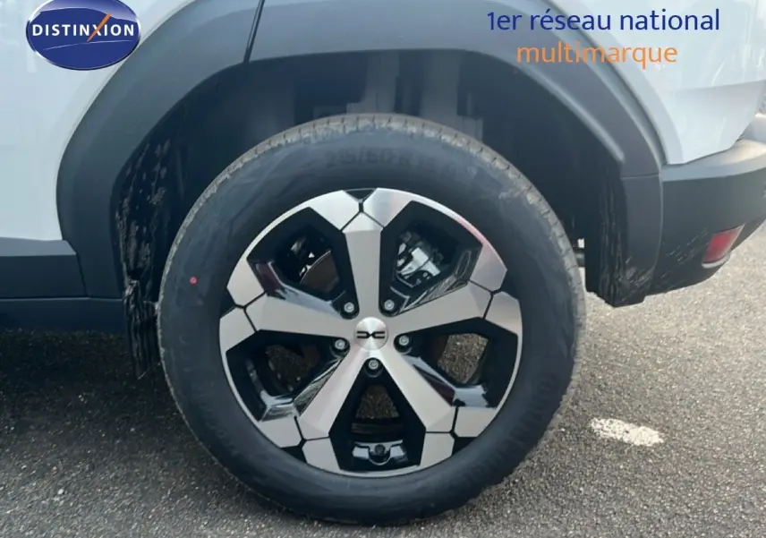 Gros plan sur la roue arrière droite du Dacia Duster blanc glacier 2025 avec jante alliage bicolore distinctive.