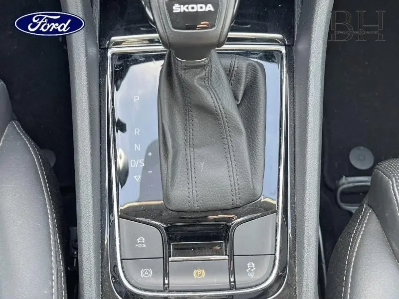 Vue rapprochée de la console centrale noire avec levier de vitesse cuir et commandes du ŠKODA KODIAQ bleu lave métallisé.