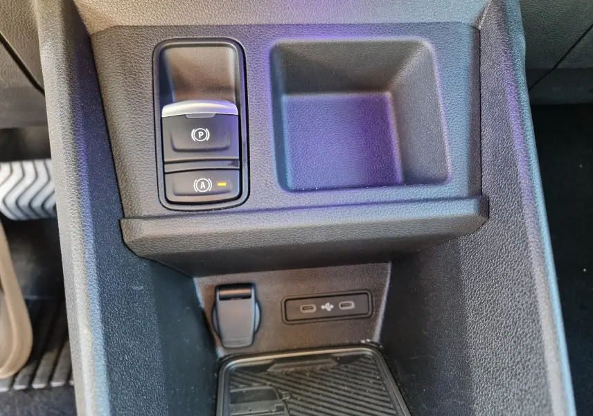 Gros plan sur la console centrale noire du Renault R5 E-TECH 2025, montrant les boutons de frein à main et arrêt auto, avec prises USB.