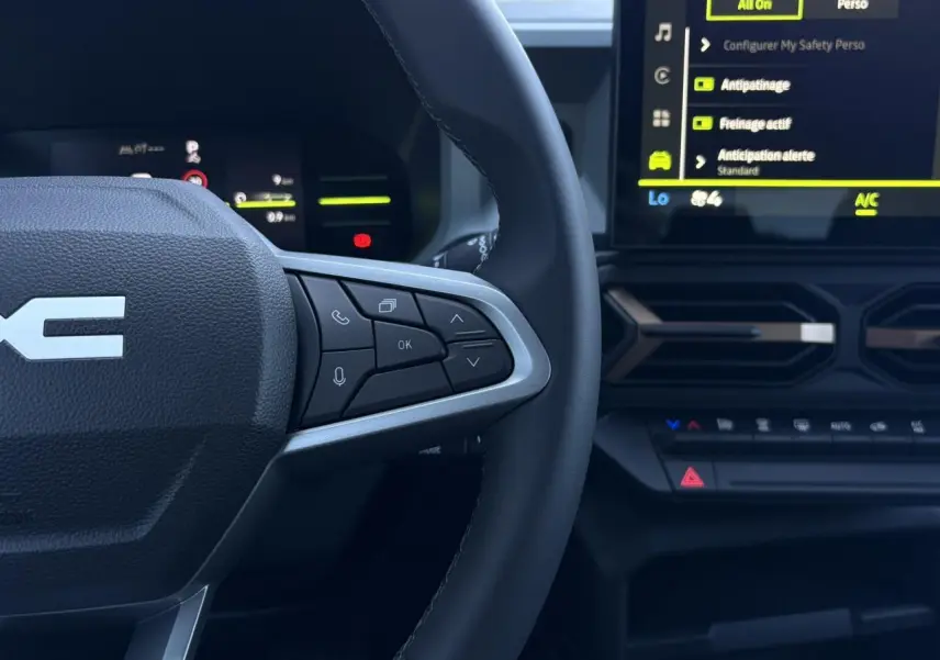 Vue rapprochée du volant côté droit et écran tactile central du Dacia Duster blanc Glacier 2026, avec commandes au volant visibles.