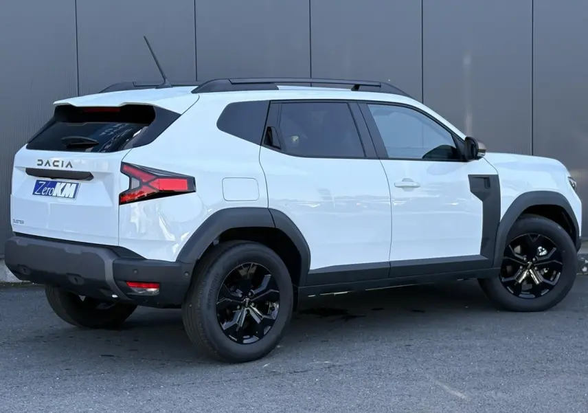 Vue 3/4 arrière droite du Dacia Duster blanc Glacier avec jantes alliage noires et barres de toit noires.