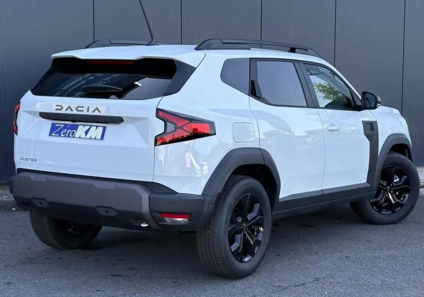 Vue 3/4 arrière droite du Dacia Duster blanc Glacier avec jantes alliage noires et barres de toit noires.