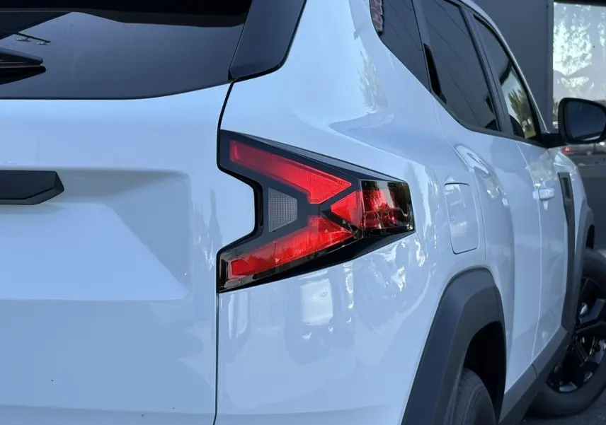 Vue arrière côté droit du Dacia Duster 2026 blanc Glacier avec feux arrière en forme de flèche et jantes noires.