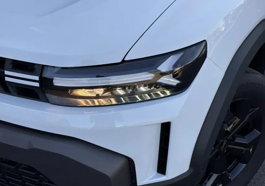 Gros plan sur l'avant droit du Dacia Duster blanc Glacier, mettant en valeur le phare LED et la jante alliage noire.