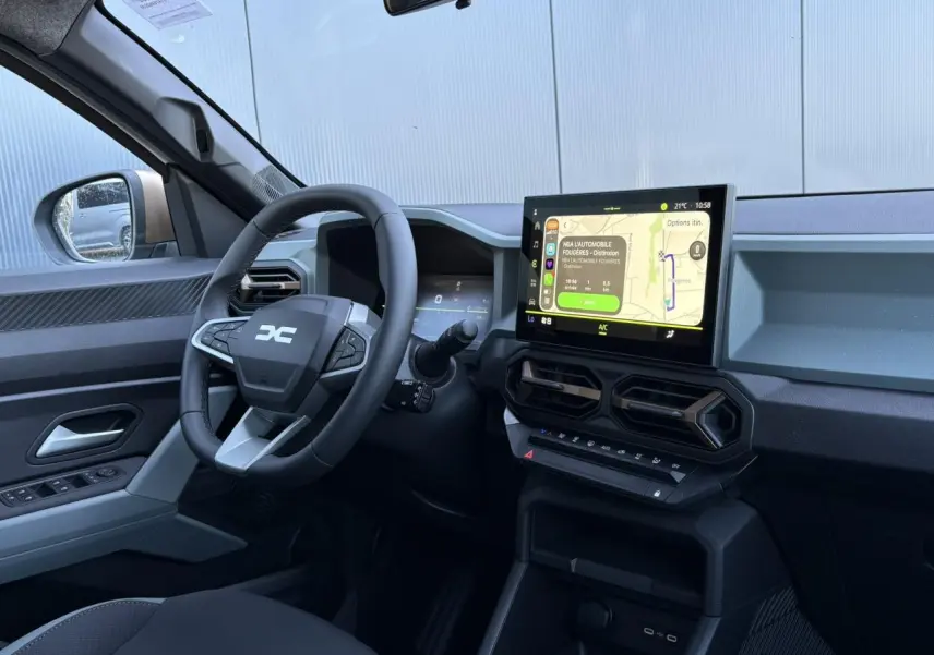 Vue intérieure côté conducteur du Dacia Duster blanc Glacier 2026, tableau de bord digital et écran tactile central visibles.
