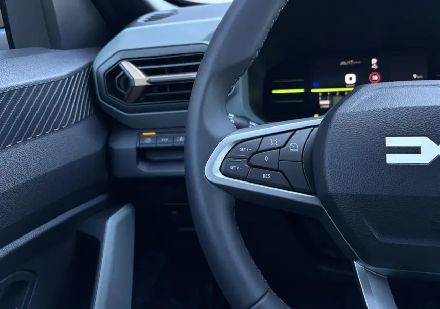 Gros plan sur le volant et la partie gauche du tableau de bord du Dacia Duster blanc Glacier, avec commandes au volant visibles.