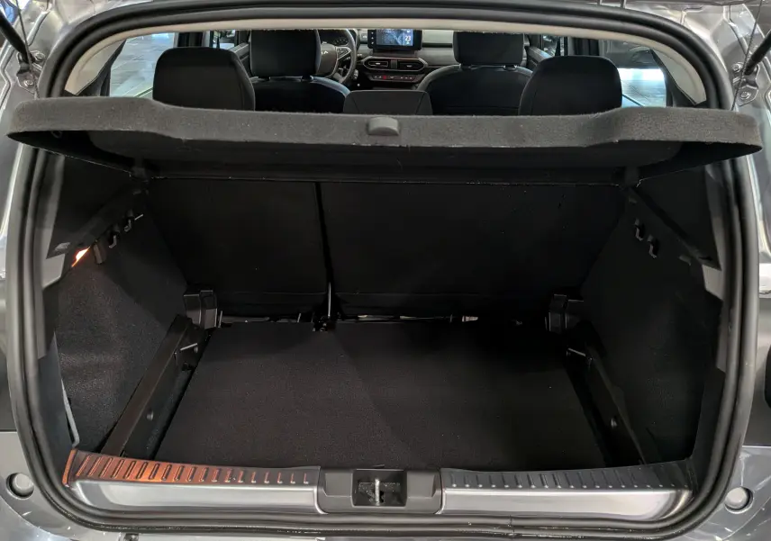 Coffre ouvert vu de l'arrière d'une Dacia Sandero Stepway 2025 gris schiste, intérieur noir et tablette arrière relevée.