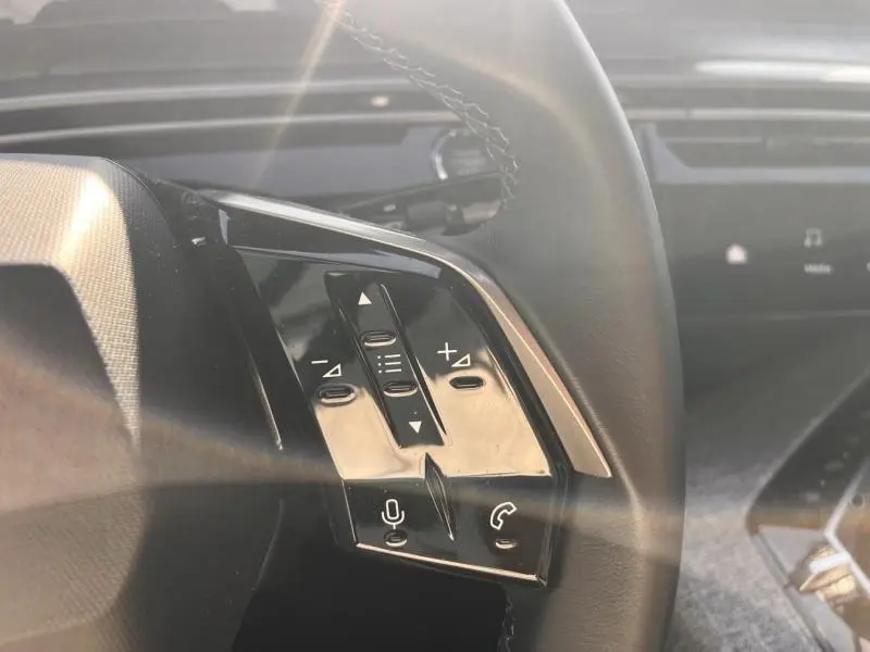 Gros plan sur les commandes multifonctions côté gauche du volant cuir du Peugeot 3008 gris Artense, intérieur moderne.