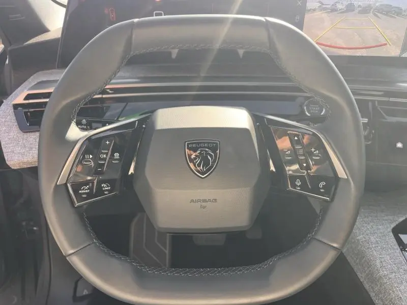 Vue rapprochée du volant cuir multifonction noir du Peugeot 3008 gris Artense avec logo lion central et commandes intégrées.