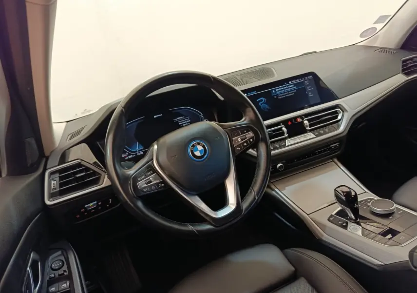 Vue intérieure côté conducteur de la BMW Série 3 320e hybride avec volant cuir, écran tactile et console centrale moderne.