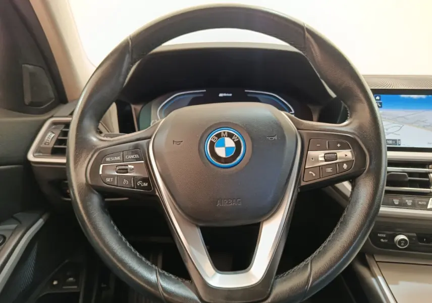 Vue rapprochée du volant cuir noir de la BMW Série 3 320e hybride avec tableau de bord numérique et écran tactile.