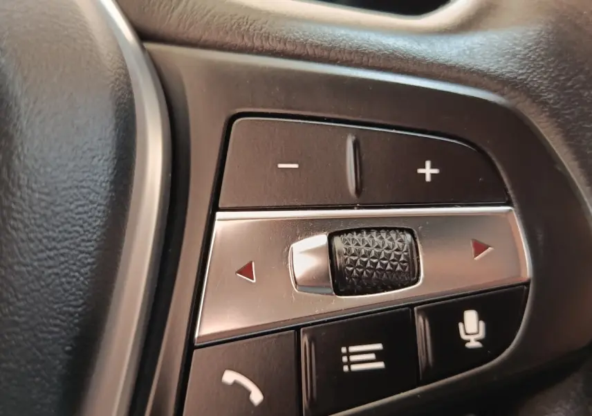 Gros plan sur les commandes multifonctions en aluminium et plastique noir du volant côté gauche d’une BMW Série 3 hybride blanche.