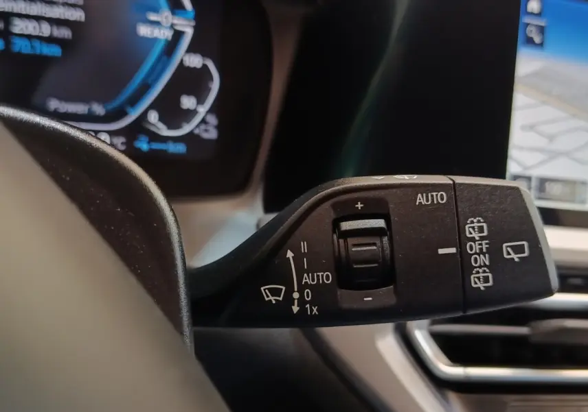 Gros plan sur la commande des essuie-glaces dans l’habitacle d’une BMW Série 3 hybride blanche, avec écran tactile visible.