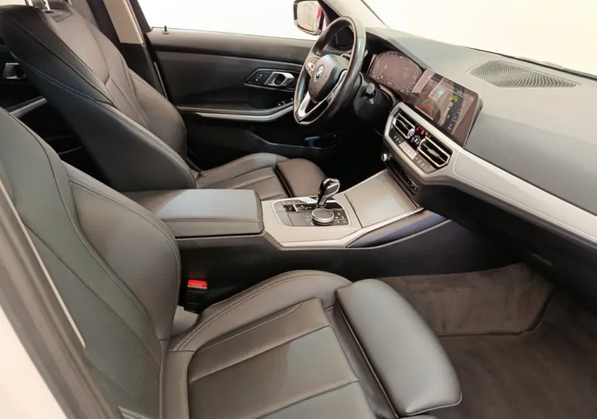 Intérieur de BMW Série 3 320e 2021 vu côté conducteur, sièges cuir noirs et tableau de bord avec écran tactile.