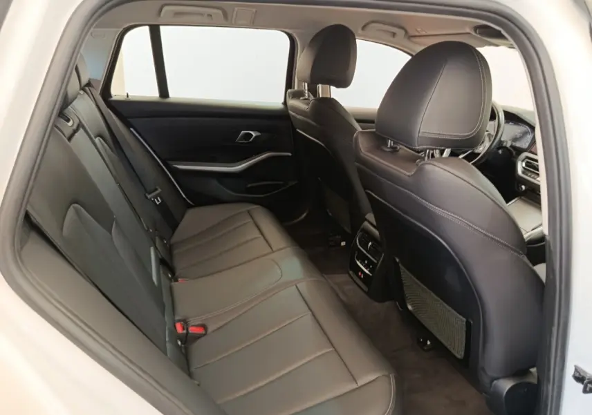 Vue intérieure arrière de la BMW Série 3 320e blanche, sièges en cuir noir et détails modernes du tableau de bord visibles.
