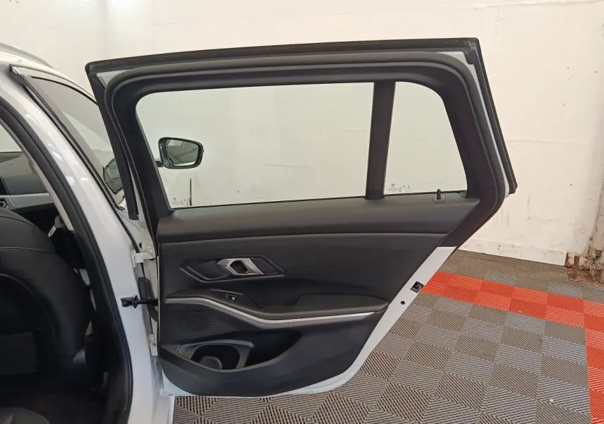 Vue intérieure de la porte arrière droite ouverte d'une BMW Série 3 320e blanche, avec garniture noire et insert alu.