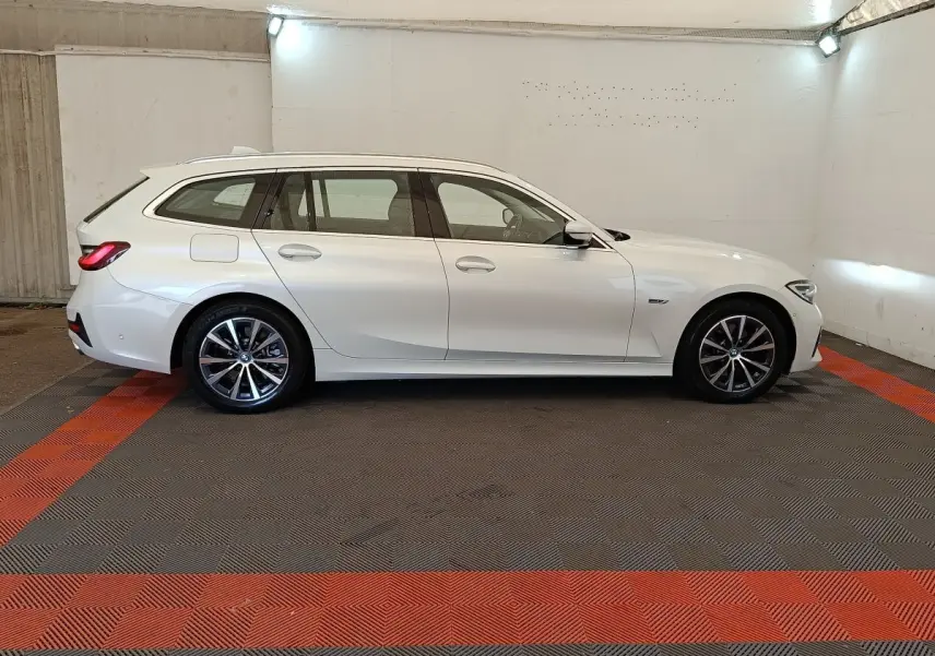 BMW Série 3 320e hybride blanche vue de profil côté gauche dans un garage avec jantes alliage noires et grises.