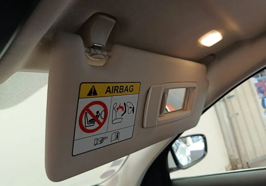 Détail du pare-soleil côté conducteur beige avec avertissement airbag dans une BMW Série 3 blanche hybride.