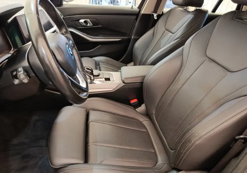 Vue intérieure côté conducteur de la BMW Série 3 320e hybride, sièges cuir noirs et volant multifonctions.