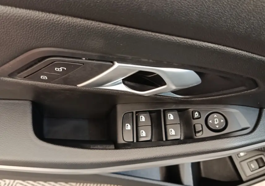 Gros plan sur la commande des vitres et la poignée intérieure noire de la porte côté conducteur d’une BMW Série 3 blanche.
