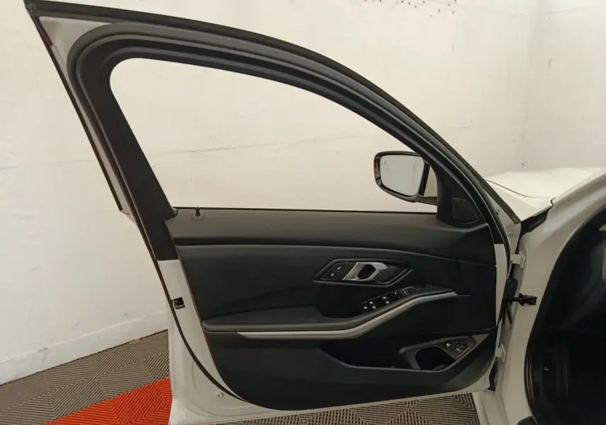 Porte avant gauche ouverte d'une BMW Série 3 320e blanche, montrant le panneau intérieur noir avec commandes électriques.
