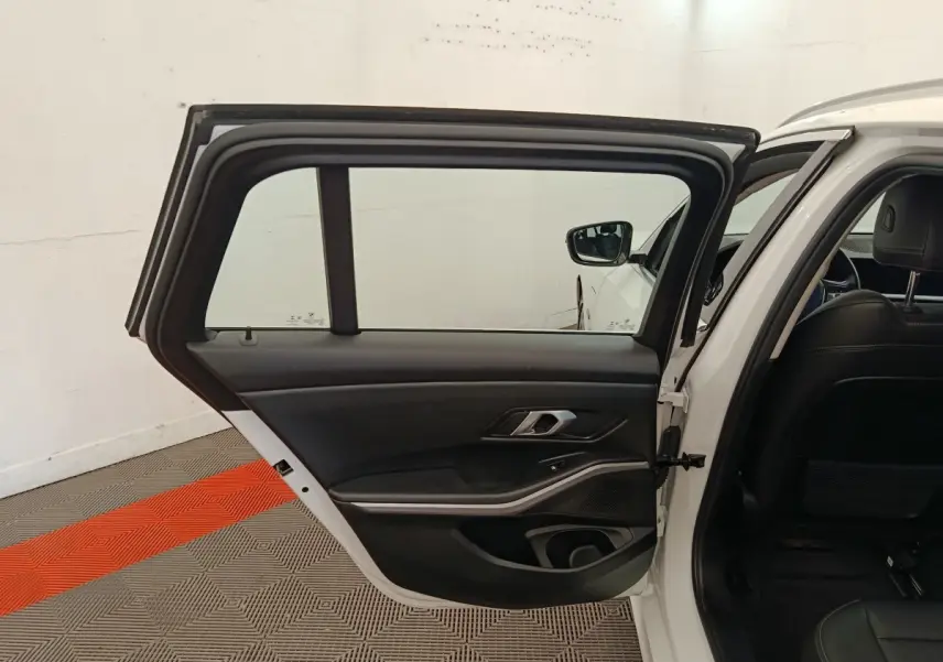 Portière arrière gauche ouverte d'une BMW Série 3 blanche, intérieur noir avec poignée métallique et haut-parleur intégré.