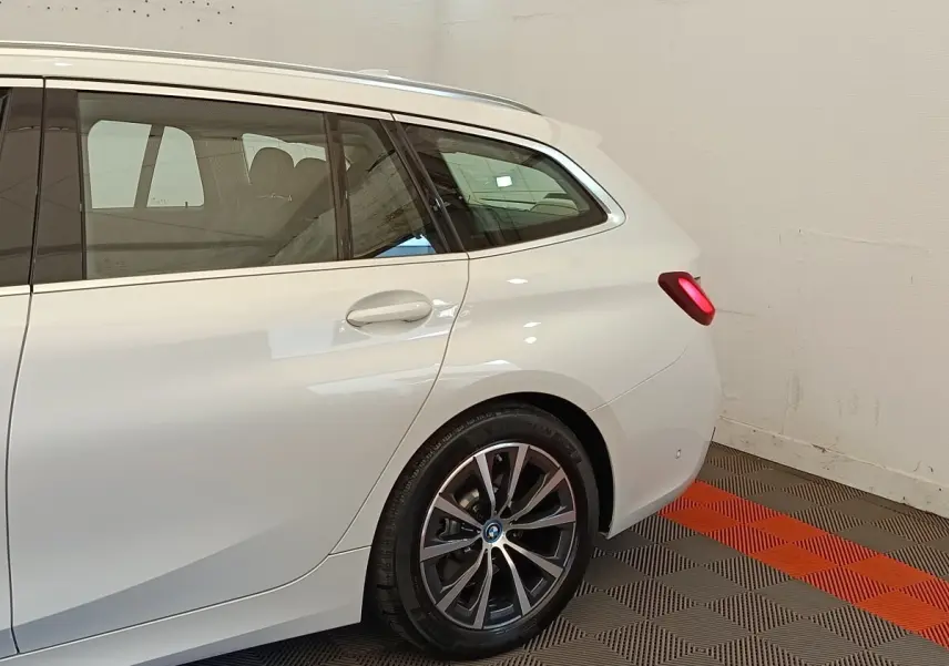 Vue arrière côté droit d’un break BMW Série 3 320e hybride blanc avec jante alliage et feux arrière allumés.