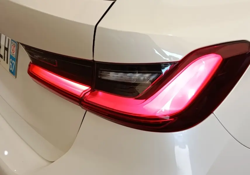 Feu arrière droit allumé d’une BMW Série 3 320e blanche, vue rapprochée du coffre et plaque d’immatriculation.