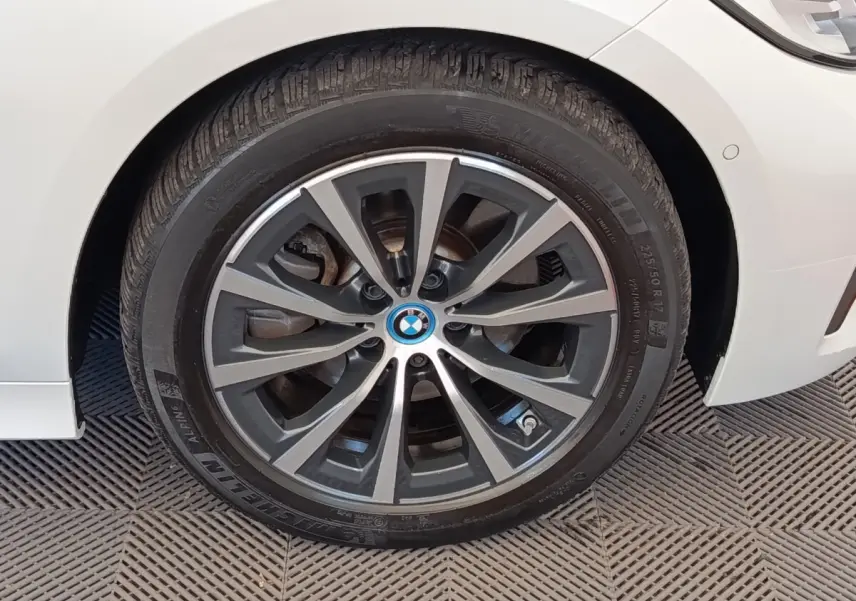 Gros plan sur la roue avant droite d'une BMW Série 3 blanche, mettant en valeur la jante alliage bicolore et le logo central.