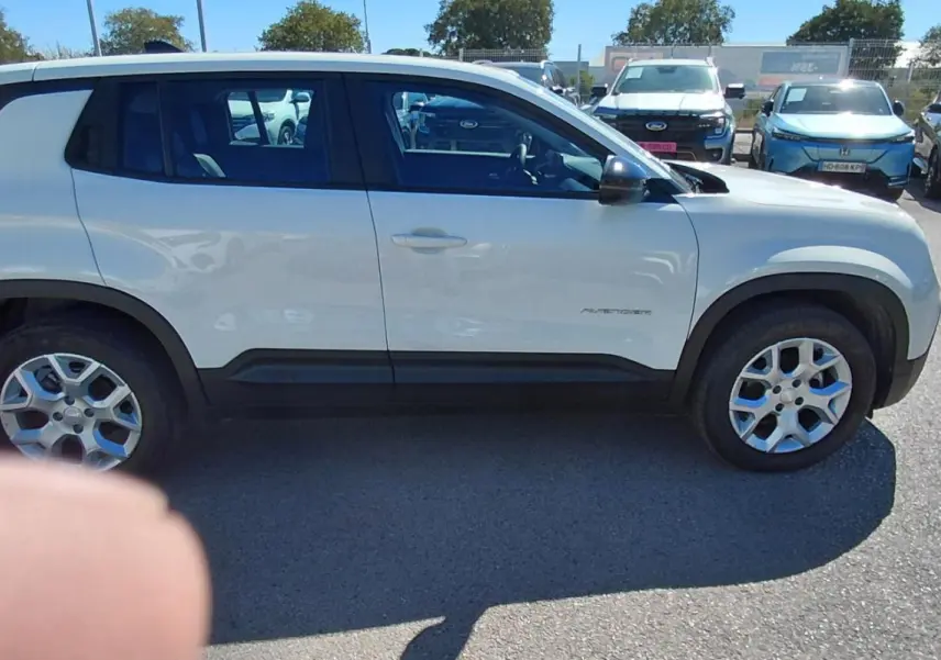 Jeep Avenger blanc vu de profil côté gauche, avec jantes alliage et protections noires sur les bas de caisse.