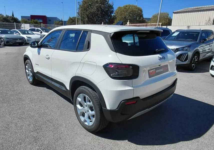 Jeep Avenger blanc vue 3/4 arrière droit, avec feux arrière sombres et jantes argentées, stationné en extérieur.