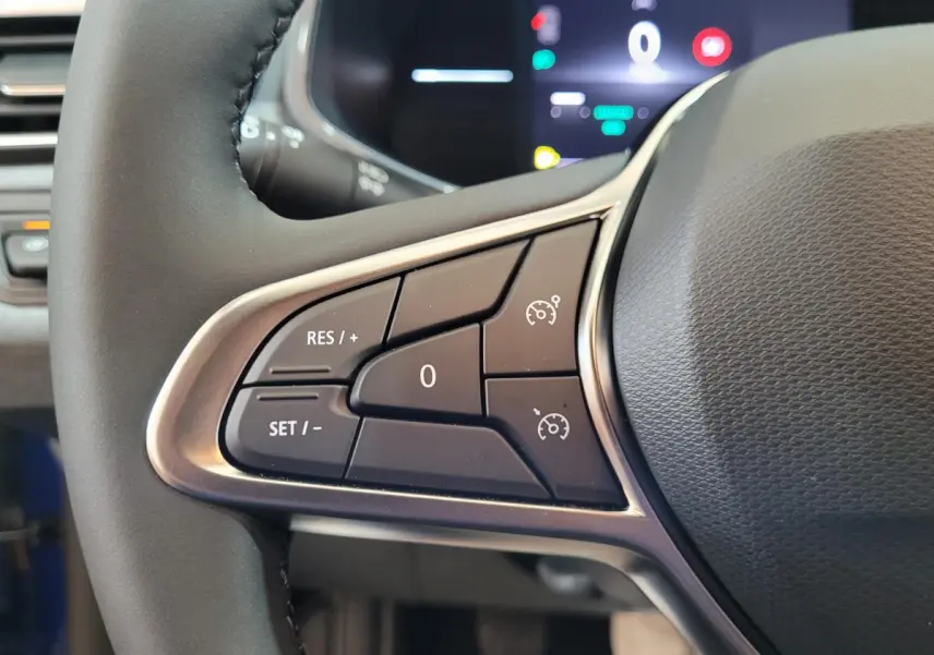 Gros plan sur les commandes du régulateur de vitesse au volant cuir noir de la Renault Clio bleu 2025.