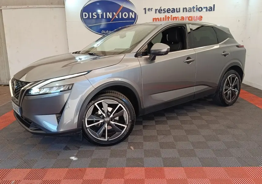 Nissan Qashqai gris foncé en 3/4 avant droit, avec jantes alliage et phares LED allumés, intérieur visible.
