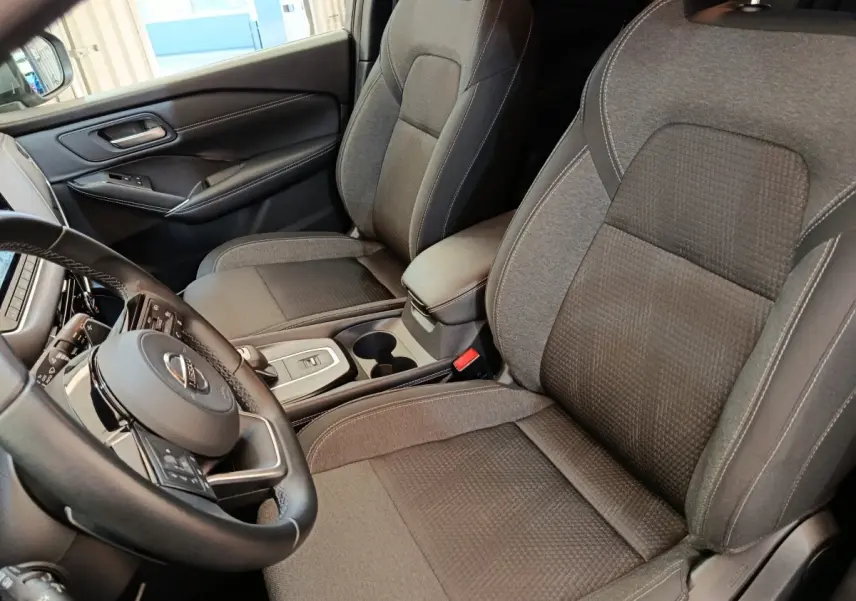 Vue intérieure côté conducteur du Nissan Qashqai 2022, sièges tissu gris et volant cuir multifonctions.